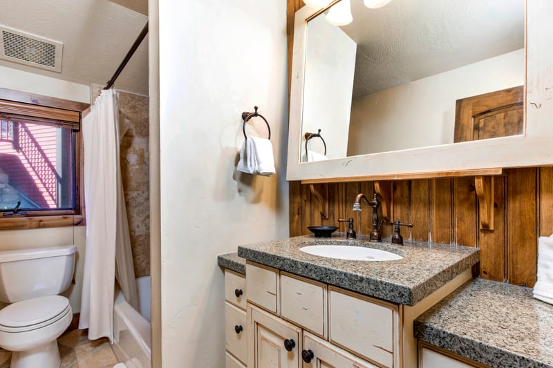 Shared bathroom with shower and tub - rustic wooden cabinets and a granite countertop is elegant.