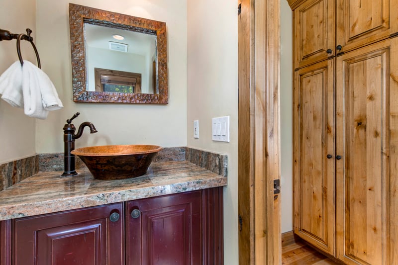 Elegant half bathroom sink area with copper bowl and wooden cabinetry charm.