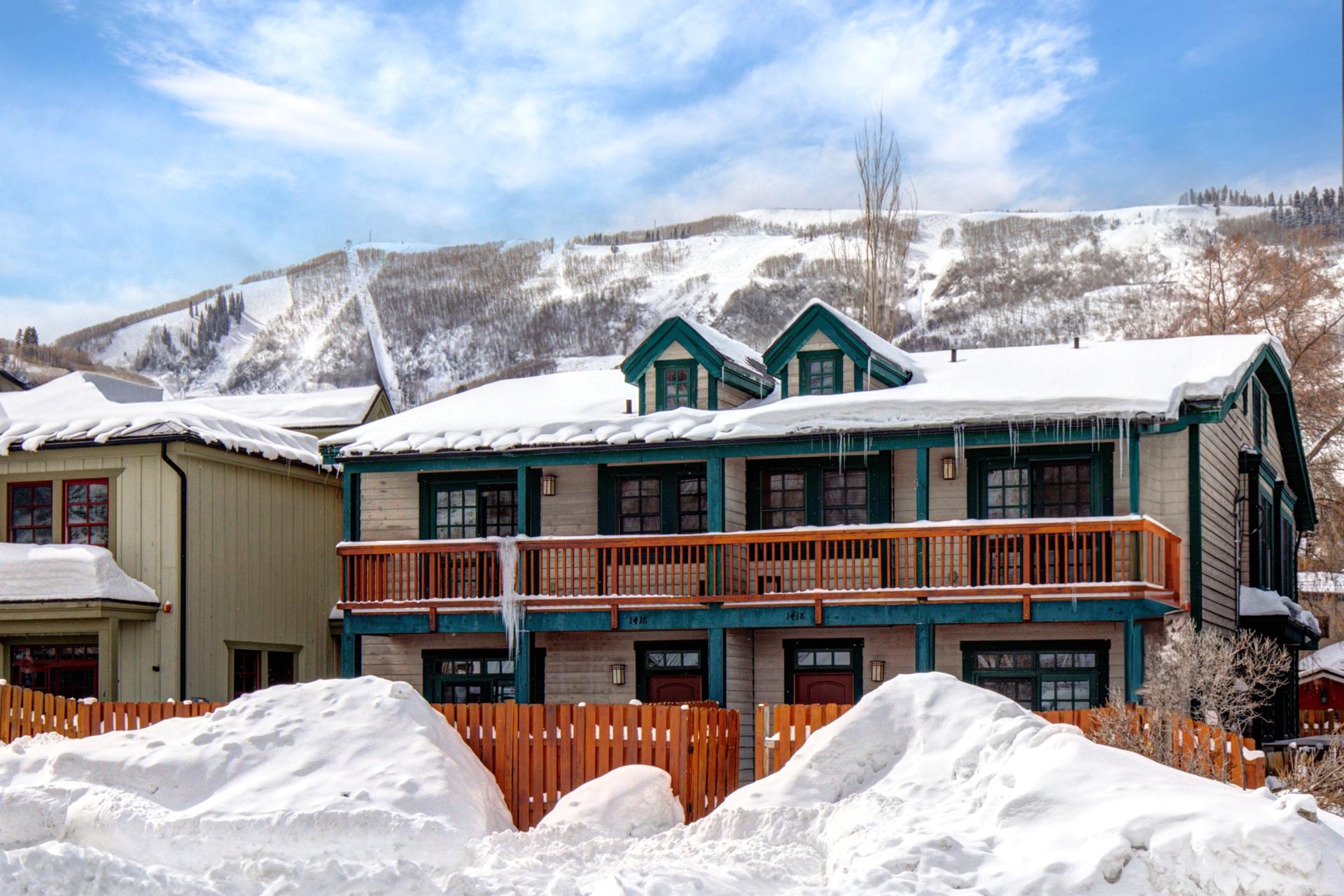 Charming duplex framed by fresh snow, wooden balconies, and a scenic mountain backdrop.