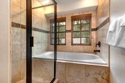Large walk-in shower with stone tile and a window view makes for a relaxing start or end to your day.