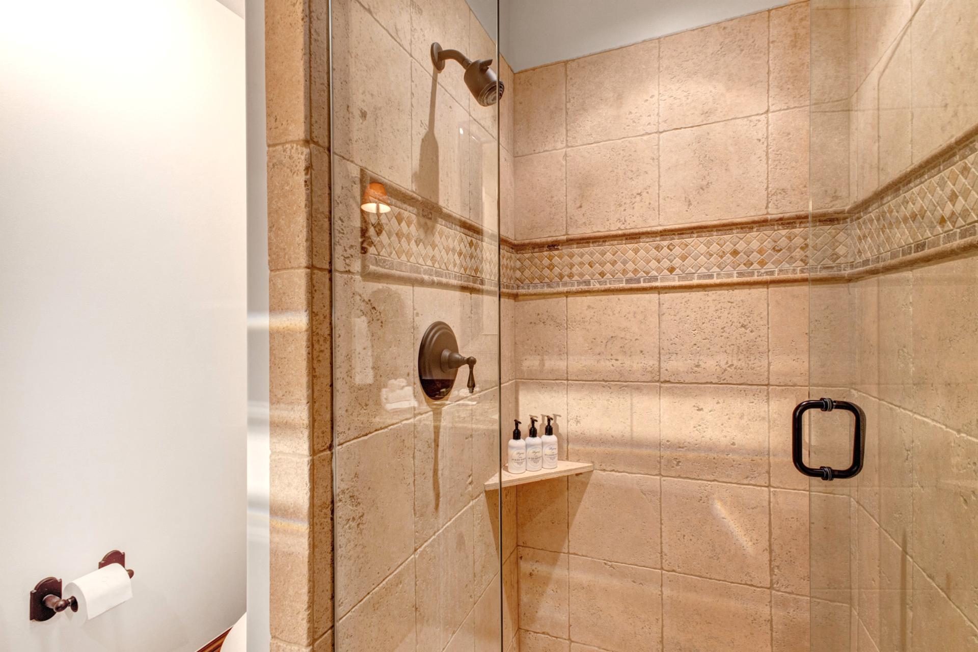 This guest bath includes a step-in tile shower and granite vanity with warm wood accents.
