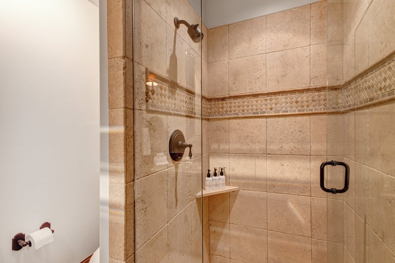 This guest bath includes a step-in tile shower and granite vanity with warm wood accents.