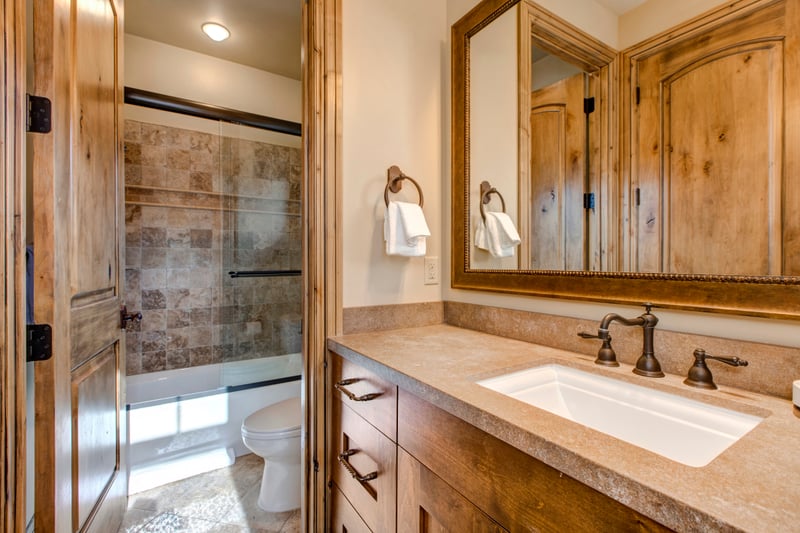 Rustic bathroom with stone tile shower, wood cabinetry, and bronze fixtures.