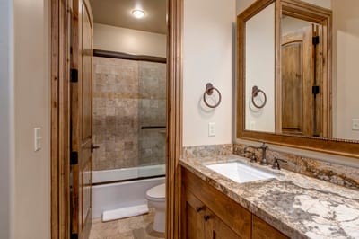 Warm rustic bathroom with granite vanity, tile shower, and wood accents.