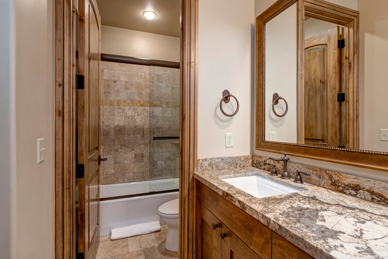Warm rustic bathroom with granite vanity, tile shower, and wood accents.