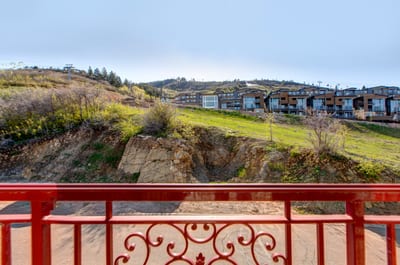 Balcony overlooks green hillside and modern mountainside residential community.