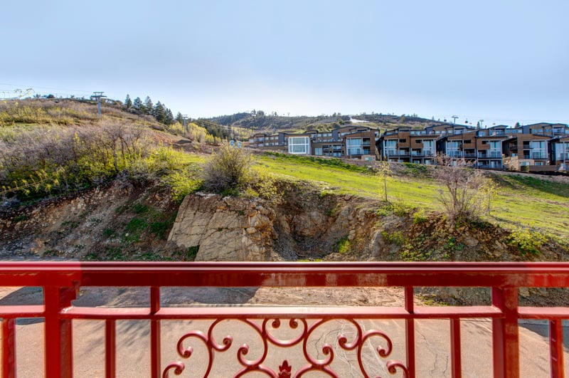 Balcony overlooks green hillside and modern mountainside residential community.